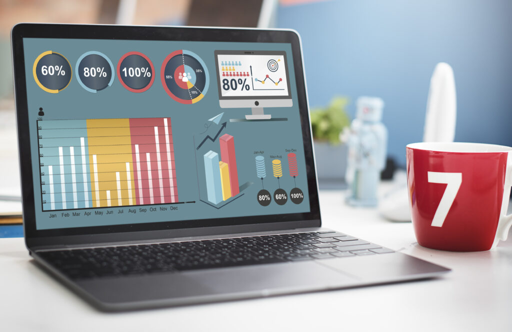 Laptop on desk displaying colorful charts and data visualizations, with a red mug labeled "7" beside it, set in a modern office environment.