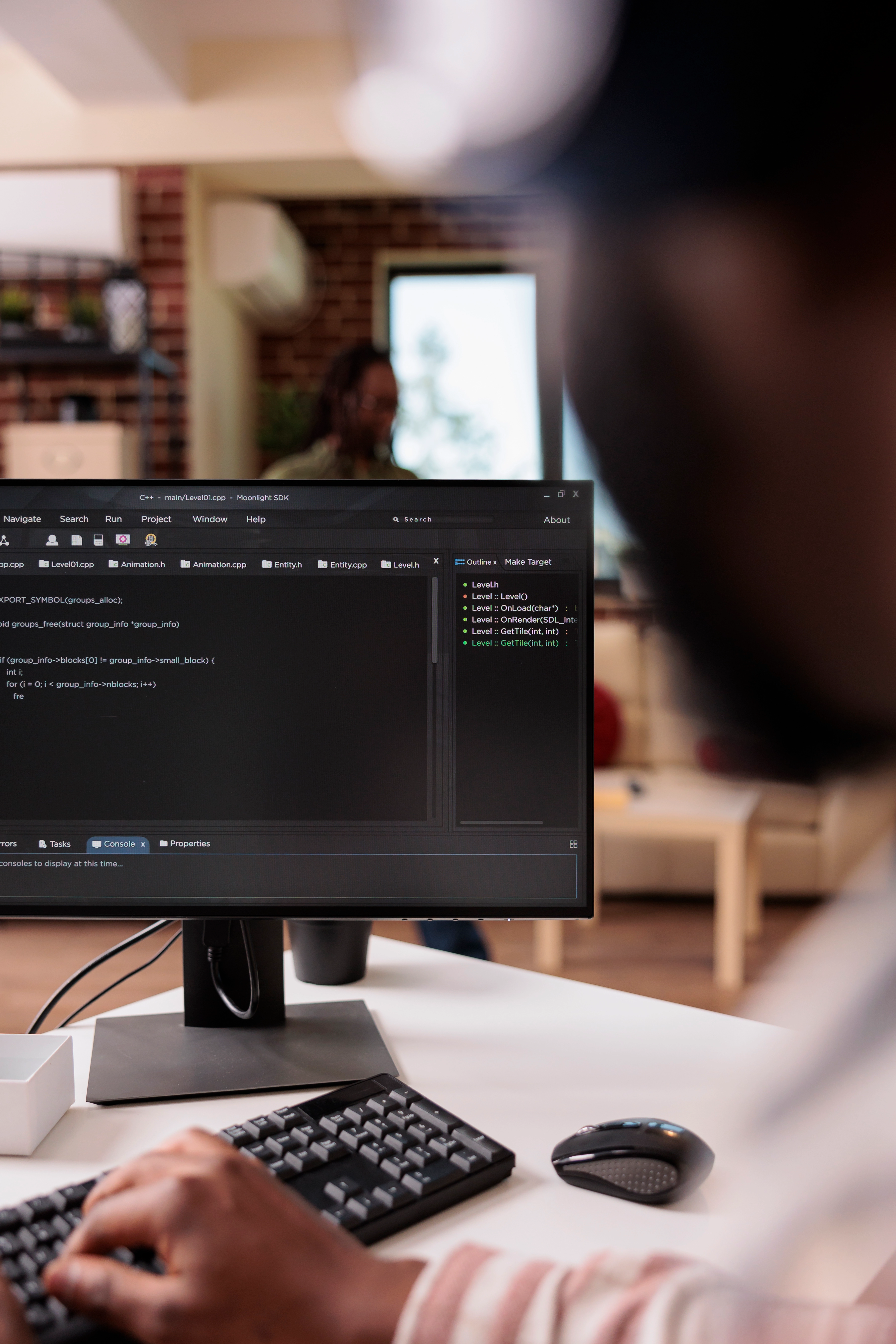 Person working at a computer displaying Python code in Visual Studio Code, set in a modern indoor workspace with shelves in the background.